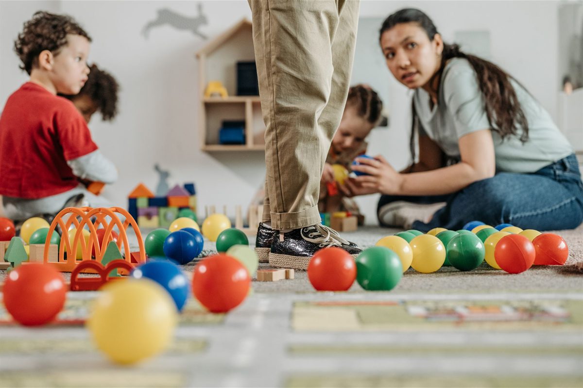 Staff member sitting on the floor beside a child at play