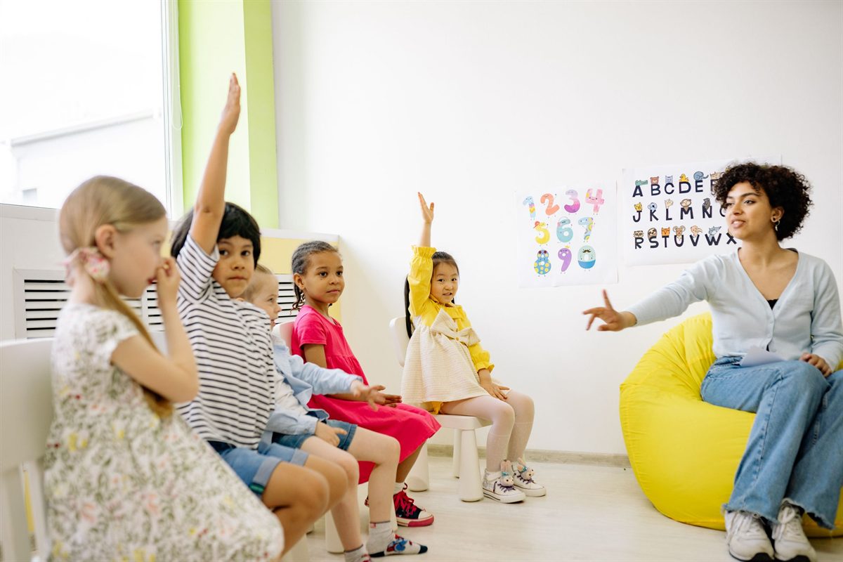Teacher giving a lesson while children raise their hands