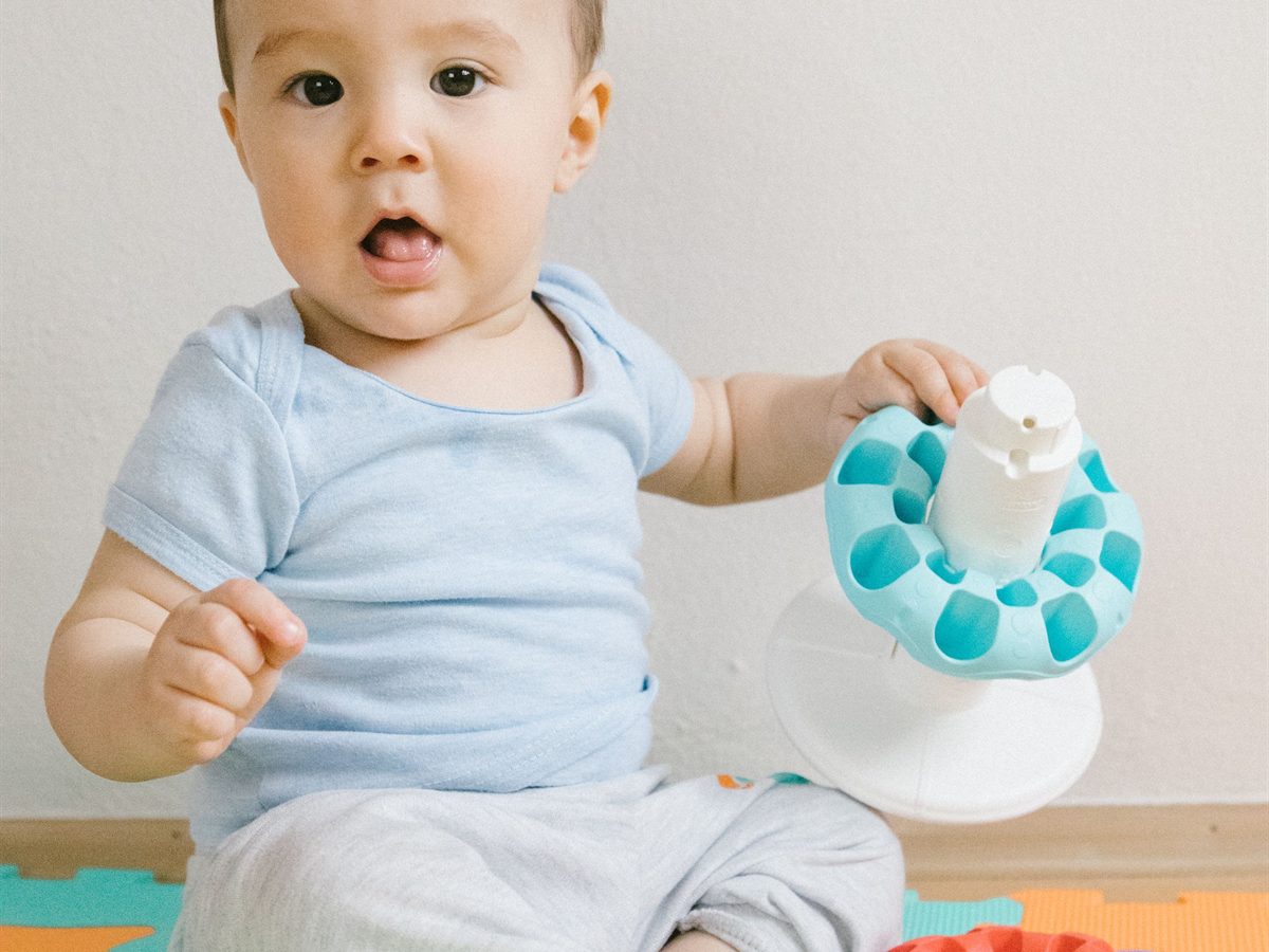 Baby sitting on a colourful play mat with toys